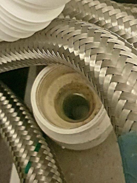 En närbild på anslutningen mellan en avloppsslang och ett vattenlås där det syns en läcka.