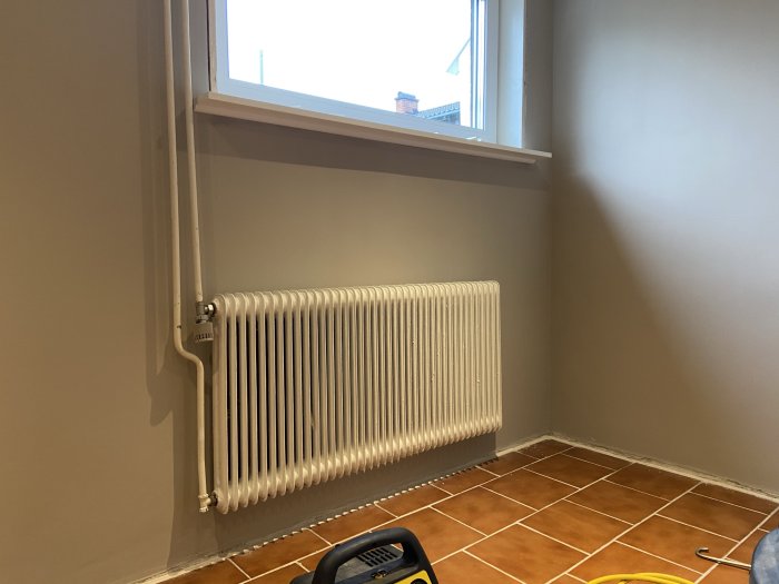 Nyinstallerad kvartsstav under en fönsterbräda ovanför en vit radiator i ett rum med terrakottafärgat golv.