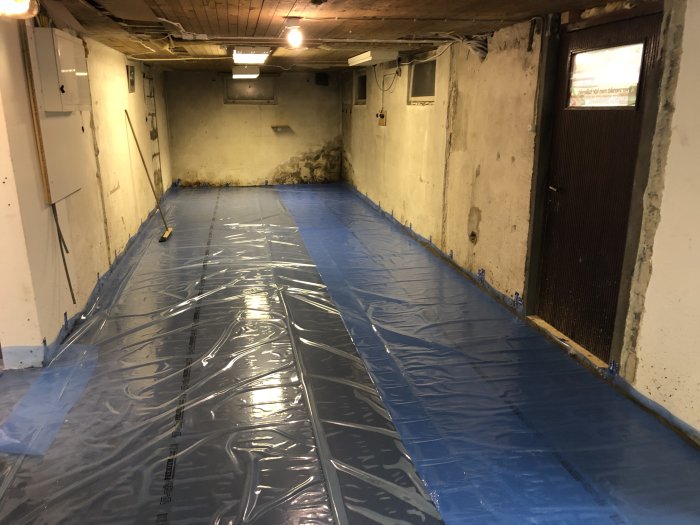 Renoverat källargolv med nyutgjuten betong täckt av blå plast för långsam uttorkning.