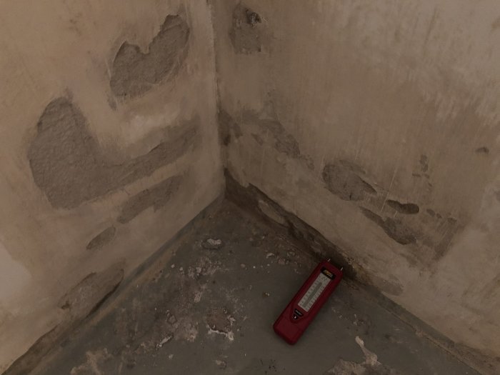 En fuktmätare mot en källarvägg med synligt fuktgenomslag och delvis lössläppt puts.