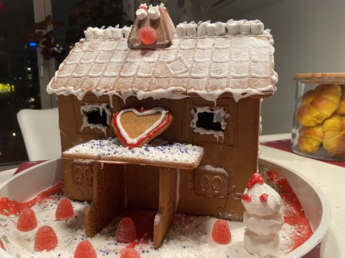 Hemgjord pepparkakshus med snödekor och en liten pepparkaksgubbe som är täckt med florsocker.