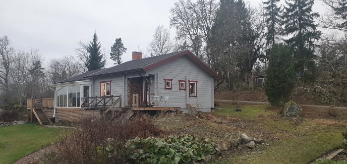 Ett grått hus med två takhöjder, en veranda, och en gräsmatta framför.