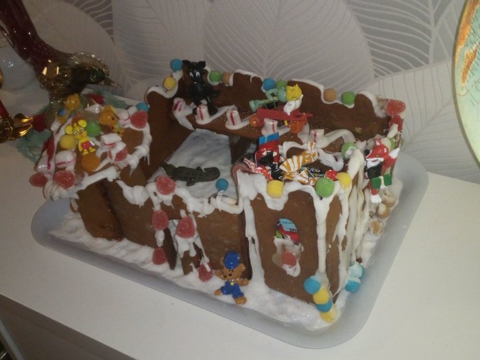 Ett hemmagjort pepparkakshus dekorerat med färgglatt godis och figurer, skapat av barn.