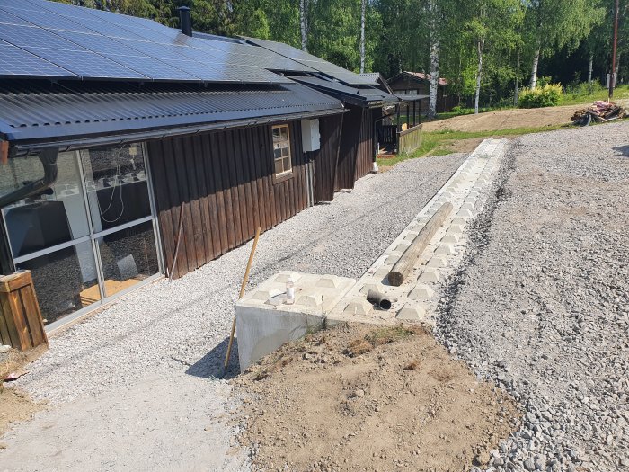 Nybyggd stödmur med betongblock från C3C intill grusad uppfart, med hus och solpaneler i bakgrunden.