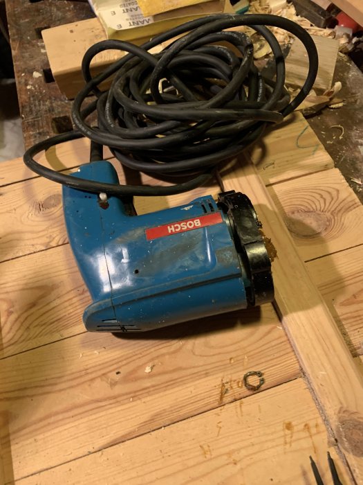 Äldre blå Bosch borrmaskin på träbänk med hoprullad sladd.