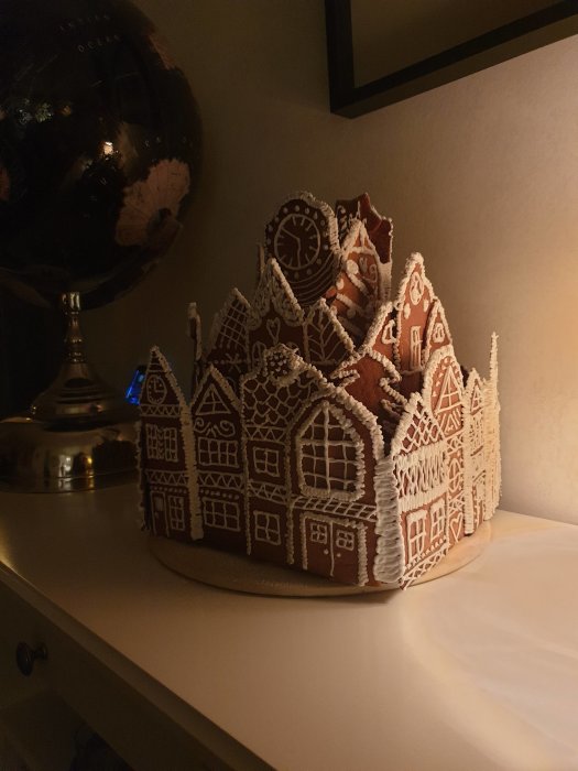 Intrikat pepparkakshus med detaljerad dekor står på ett bord intill en världsglob.