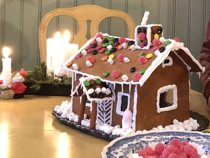 Pepparkakshus dekorerat med godis och marsipan på ett bord med ljus och tomtedekorationer.