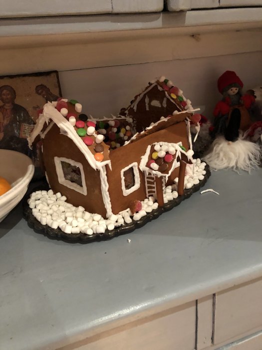 Pepparkakshus med kollapsat tak och dekorationer av godis och kristyr på ett bord.