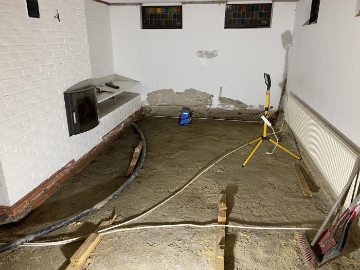 Källare under renovering med uppbruten golv, fuktskador på vägg och en synlig kabel på marken.