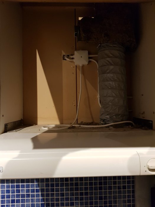 Äldre köksfläkt monterad ovanför kakel, med synlig ventilationskanal och elanslutning, i behov av en uppdatering.