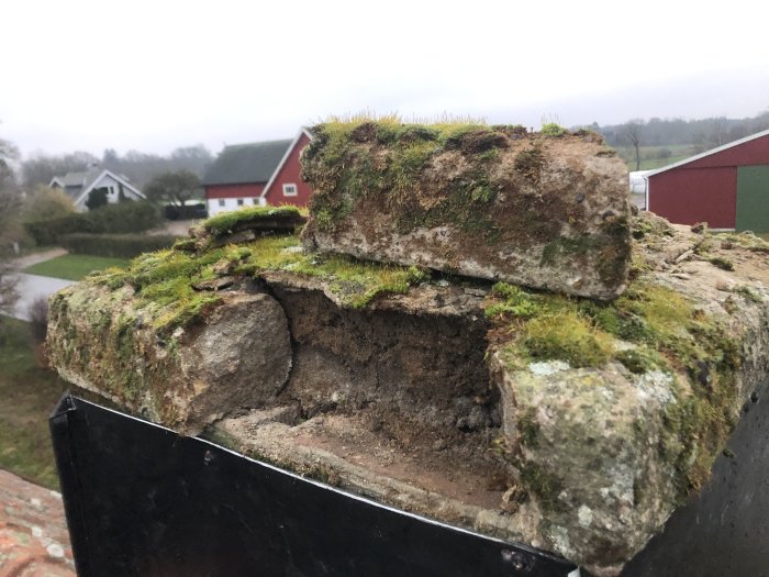 Närbild på toppen av en skorsten med söndervittrat murbruk och mossa, markerad för reparation.