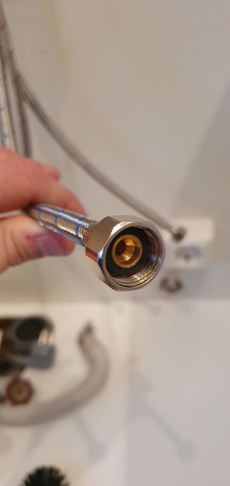 Närklädsel på en flexibel VVS-slang med G 3/8 invändig gänga och synlig packning hållen i en hand, otydlig bakgrund.