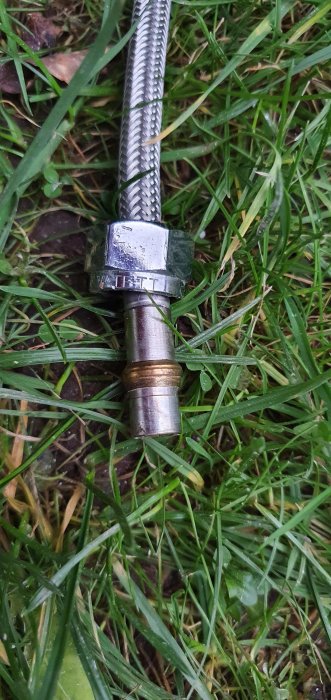 Vattenanslutningsslang för blandare med metalländar och utvändig gänga liggande på gräsmatta.