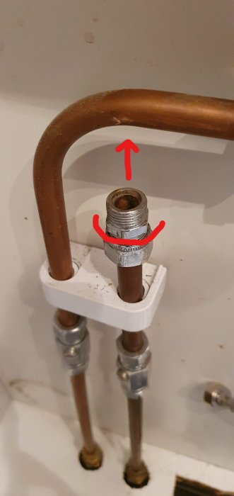 Kopparrör med klämringskoppling markerad med röd pil och ring för att visa övre delen som ska skruvas loss.