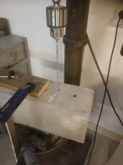 Borr i pelarborrmaskin genomför borrning i en betongmursten med synlig borrspån och verktyg i bakgrunden.