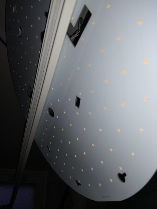 Undersidan av en rund ledpanel i taket som visar flera tända ljuspunkter och två svarta hål.