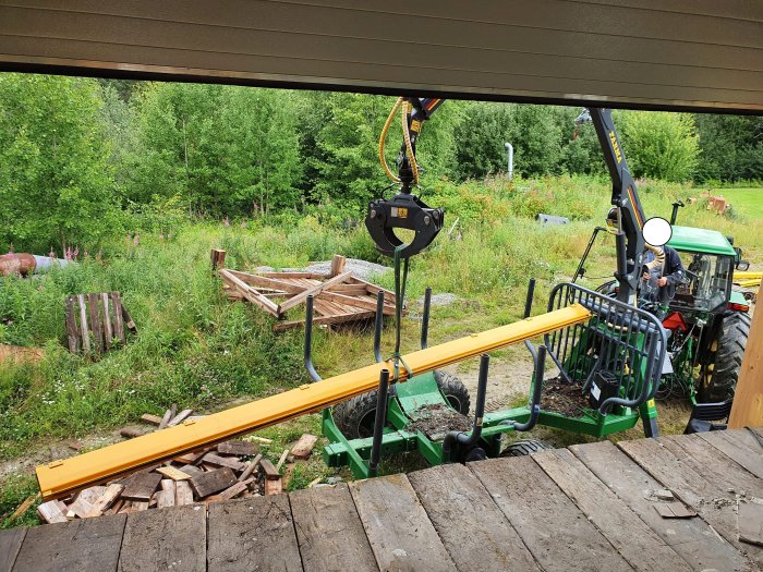 Gul lyftbalk på travers monteras utomhus med hjälp av grön traktor och kedjeblock.