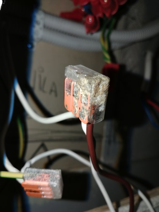 En närbild på en transformator med brända och smälta delar i ett elsystem, omgiven av olika färgade kablar och kopplingsklämmor.