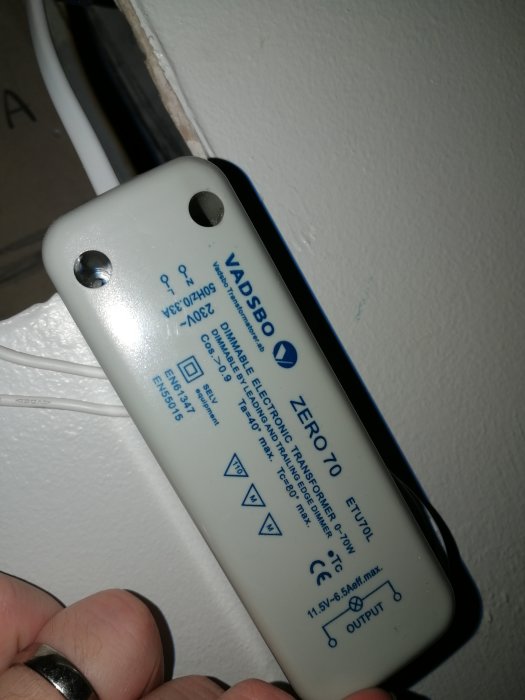 Hand håller en elektrisk transformator märkt med 'ZERO70 ETU10L' för 12V 20W halogenlampor som kan vara defekt efter 'elsurr'.