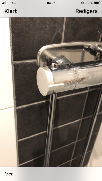 Kromad okänd blandare monterad på väggen intill gråa kakelplattor, synlig temperaturknapp saknas.