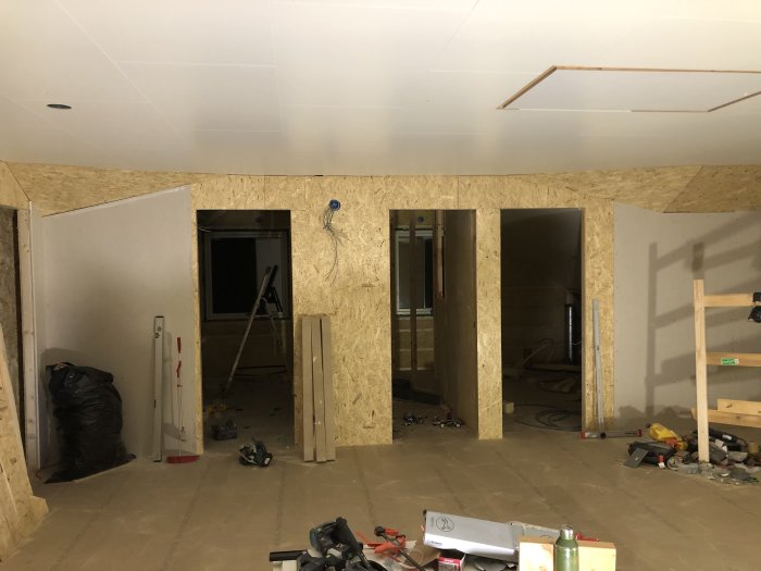 Ovanvåning under renovering med osb-skivor på väggarna och gipstak, samt byggmaterial utspritt på golvet.