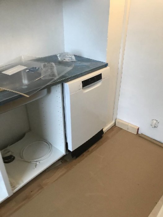 Diskmaskin intill en vägg med synlig kabelkanal, inget mellanrum mellan maskin och vägg, köksskåp och arbetsbänk syns också.