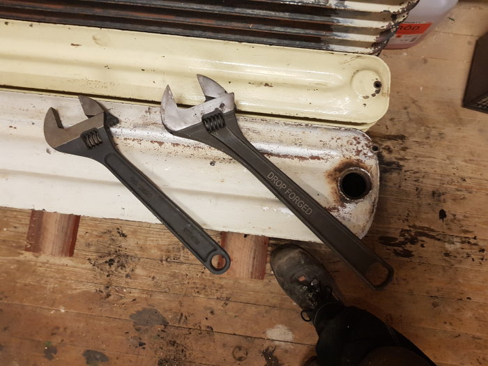 Två skiftnycklar i olika storlekar på ett slitet trägolv bredvid en radiator.
