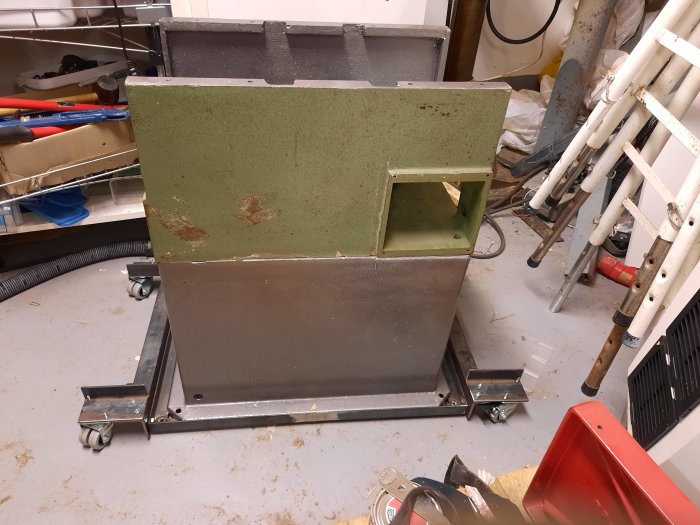 Grön och grå metallstruktur på hjul, ser ut som en del av en maskin i en verkstad.
