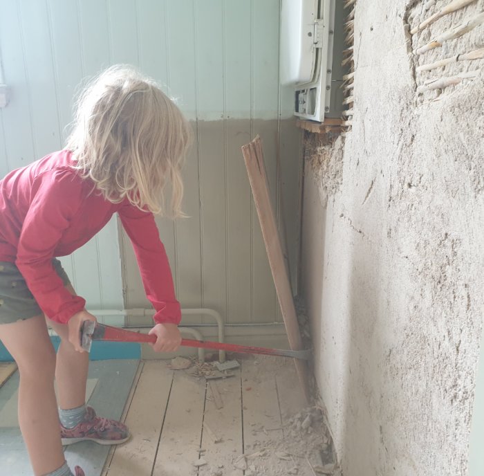 Barn deltar i husrenovering genom att riva en gammal vägg med lerklining.