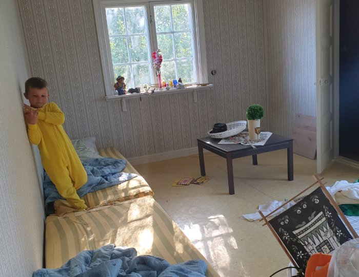 Barn i Pikachu-pyjamas i ett rum med möbler och leksaker under renovering.