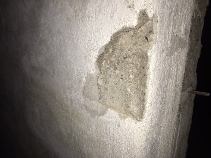 Grovt putsat källarvägg med synlig reparation och spricka, behov av slätning och målning.