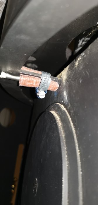 Elledning fäst vid svart metallstruktur med slangklämma, noga placerad för att undvika kontakt med isolering.