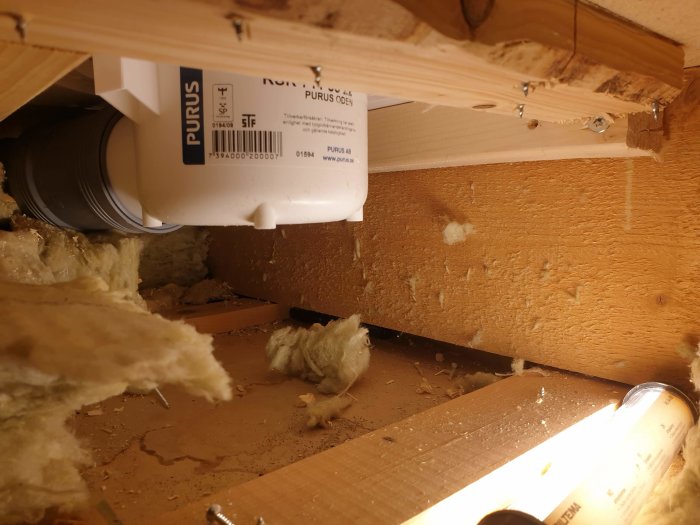 Felaktigt installerad golvbrunn under golv med synliga rörgenomföringar och spridd isolering.