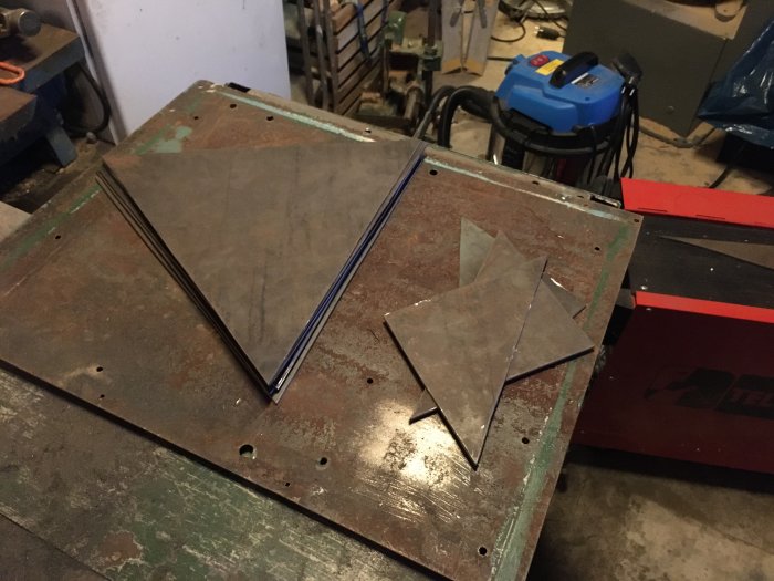 Sexkantiga metallplåtar och trianglar på verkstadsbord, prototyp för hemsydd eldskål.