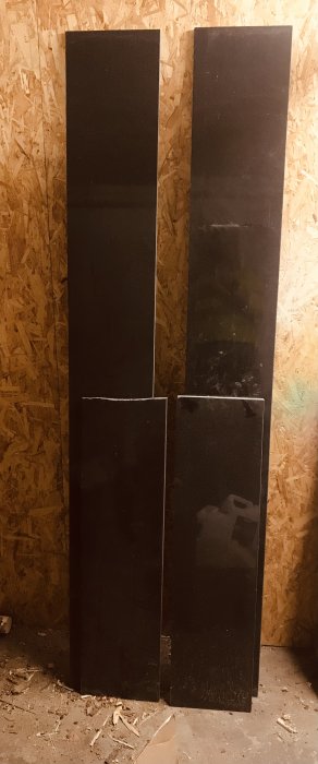 Fyra svarta granitfönsterbänkar i olika längder, uppställda mot en OSB-skiva med spån, i ett rörigt rum.