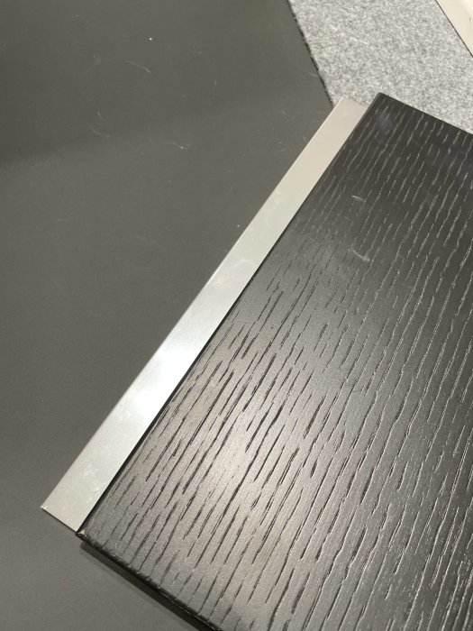 Svart ek-skiva från Ballingslöv Line med kantlist i aluminium mot grå bakgrund.