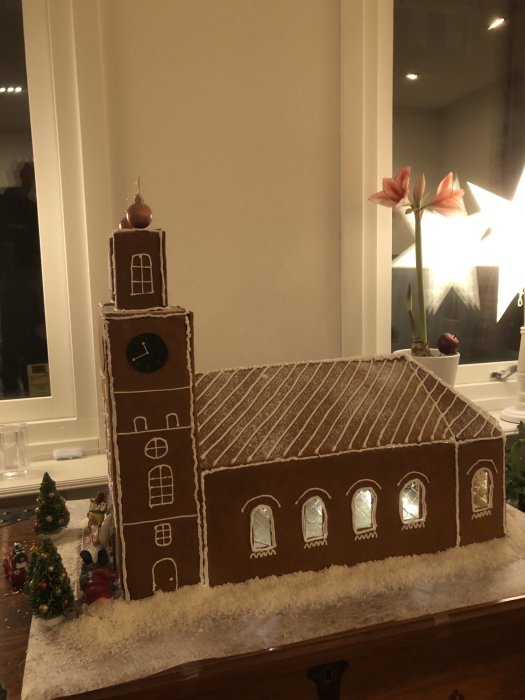 Pepparkakshus som liknar en kyrka dekorerad med kristyr, omgiven av juldekorationer.