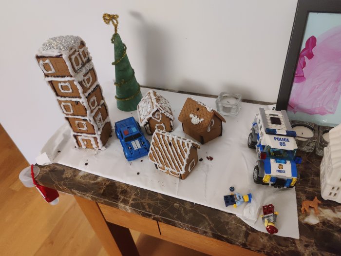 Modell av stad med pepparkakshus i form av skyskrapa, villor, ett ödehus, LEGO-polisbil och figurer.