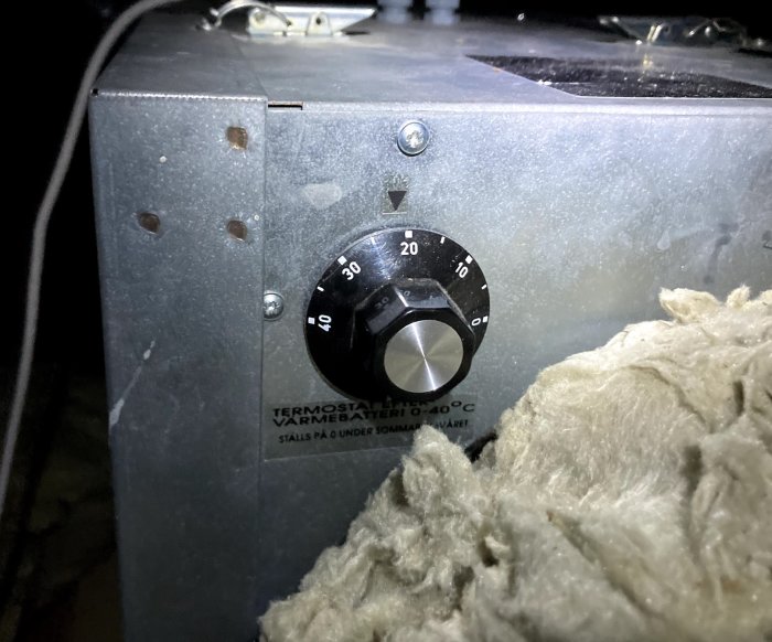 En termostatknapp på ett gammalt Flexit VGL-400 ventilationsaggregat, omgiven av isoleringsmaterial.