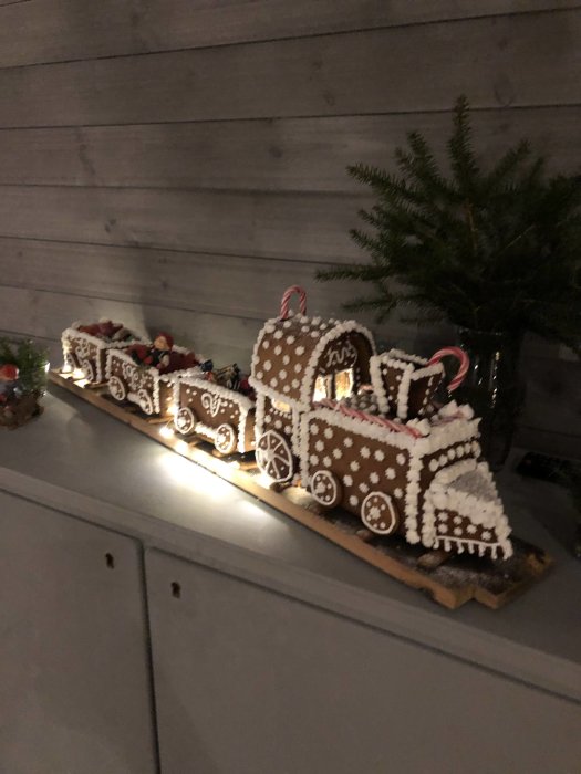 Pepparkakståg dekorerat med kristyr och godis står på ett bord, invid en gran.