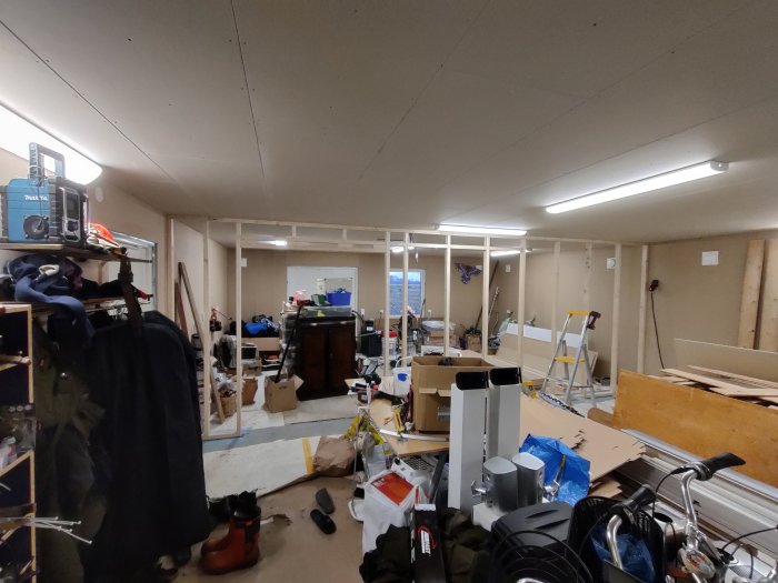 Garage under konstruktion med mellanvägg och träpanel, rörig inredning och en julgran.