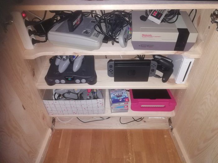 En hylla med blandade spelkonsoler inklusive en Nintendo Switch, SNES och originalet Nintendo Entertainment System.
