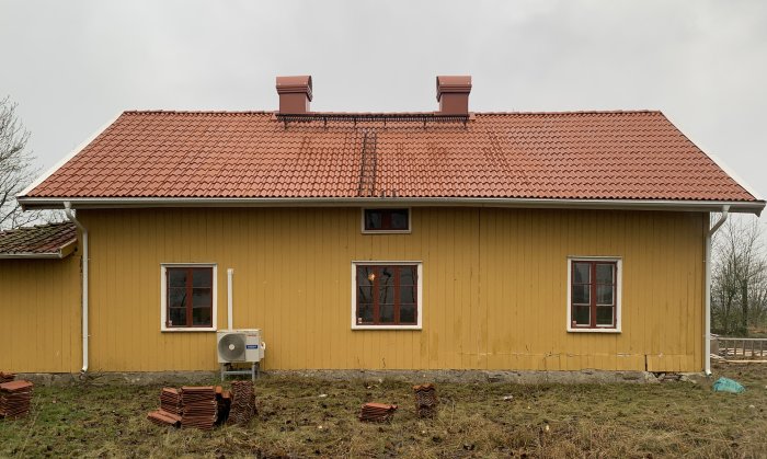 Nyrenoverat tegeltak på ett gult hus med en viss ojämnhet i taklinjen som ger karaktär.