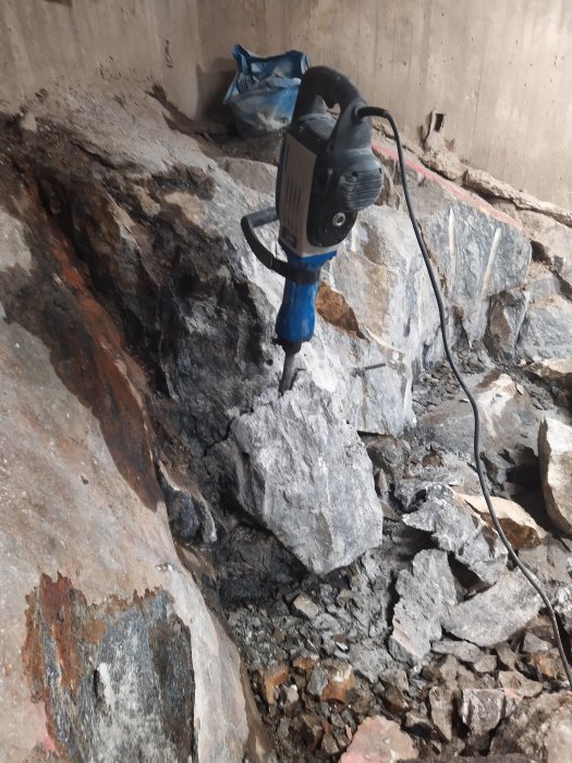 Bilhammare på stor stenblock i bergdelen, spräckt berg och lösa stenar synliga.