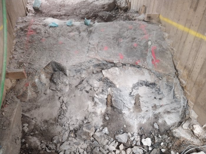 Spräckt berggrund med stora och små stenblock och borrade hål, markerat för ytterligare arbete.