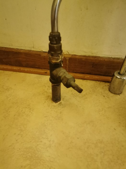 En gammal koppling på ett kallvattenrör med en sidoutrustning som kan vara en vattenstrypare eller en pluggad T-korsning.