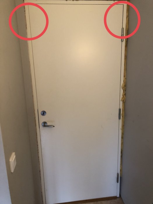 En skev vit dörr som tar i karmen uppe till vänster, med synliga gångjärn och skruvar.
