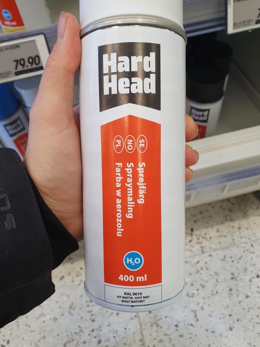 Hand håller en sprayburk med färg på Jula, vit matt färg, Hard Head märke.