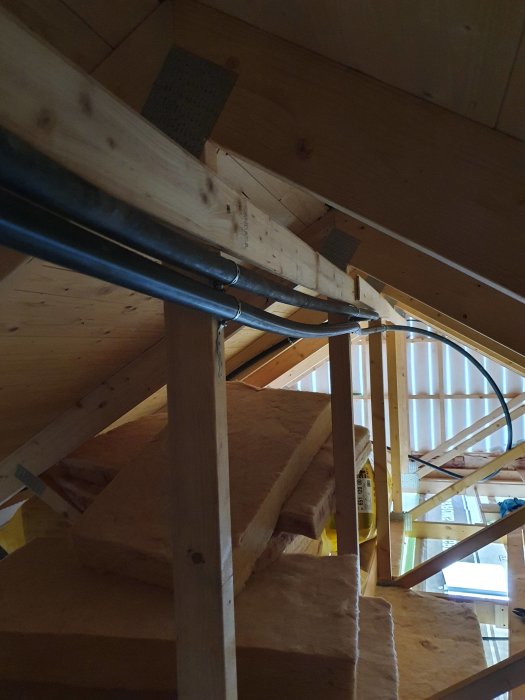 Del av en byggkonstruktion inuti ett garage med isoleringsmaterial i taket och PEM-slangar längs takbjälkar.