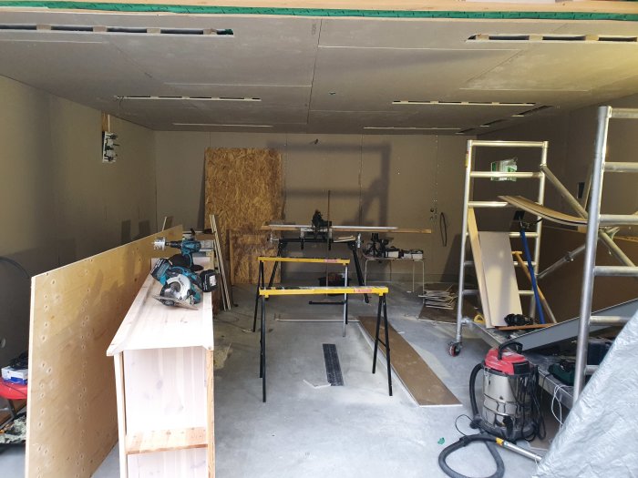 Garage under renovering med gipslyft, verktyg och delvis monterade gipsskivor på tak och väggar.